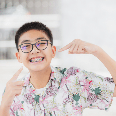 Caring for braces and aligners: orthodontic essential tips 11 Little boy wearing glasses, smiling and pointing toward his braces, representing orthodontic treatment